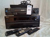 Front view of Onkyo receiver, JVC VCR, Samsung Blu-ray player stacked with three remotes visible