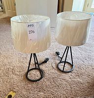 Pair of black metal tripod lamps with white shades, cords visible