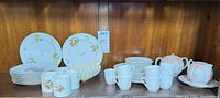 Mixed china plates, cups, cream & sugar set on wooden shelf