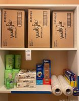 Shelf with three Vanity Fair cartons, assorted wipes, sanitizer, napkin packs, Ziploc boxes, stretch film rolls, Reynolds wrap