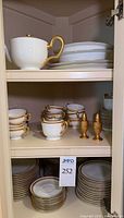 Stacks of plates, cups, teapot, serving pieces and metal shakers on cabinet shelves
