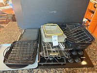 Overview of nested enamel roasting pans, wire racks, fry basket, grill plates and baking pans