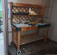 Full view of wood potting bench with lattice back, metal top, wheels and tools displayed