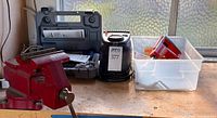Lot overview showing red bench vise, grey Dremel case, black Craftsman inflator and clear bin with red Remington tool