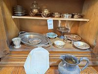Cabinet view showing majority of silver-plated pieces including trays, bowls, compote, holder, pitcher