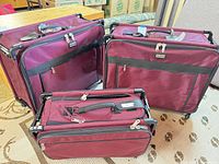 Three burgundy Tutto rolling suitcases, two medium and one carry-on