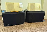 Pair of black Bose 301 Series IV speakers with cream Bose Model 100 speakers placed on top