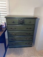 Front view of green tall dresser showing five drawers, hardware and carved applique