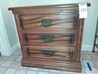 Front view showing three drawers with ornate handles and plinth base