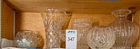 Shelf view of four crystal pieces including rose bowl, flared vase, cylindrical bowl and globular vase