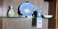 Shelf with green bud vase, blue commemorative plate on stand, blue flared vase, stack of two white pin dishes