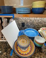 Stacks of blue dinner and salad plates with yellow/blue bowls, patterned plates and bowls visible