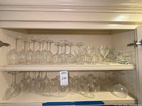 Two shelves with assorted clear wine glasses, cut-glass goblets, and small bowls