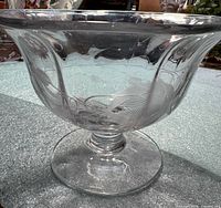 Angled side view of clear glass compote on pedestal showing full form and etched floral design