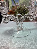 Front view of clear pressed glass double candlestick holder showing ornate scroll arms and round foot