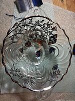 Nested view of both clear glass bowls showing scalloped rims, sterling silver poppy overlay, handles and feet