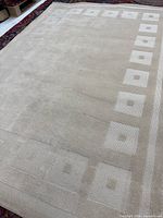 Full view of beige wool rug showing size and border pattern