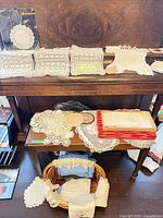 Overview of assorted doilies, table runners, linen napkins and packaged paper doily set displayed on furniture