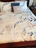 Full view of queen bed showing duvet cover, shams and two decorative pillows with floral botanical design
