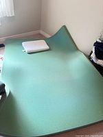 Green memory foam topper spread on floor with white pillow on top