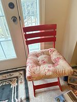 Red wooden folding chair with floral cushion positioned near door