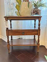 Front view of brown wood veneer end table showing top, drawer with circular pull, and two shelves