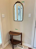 Wall mirror mounted above matching wood demi-lune table in corner