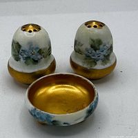 Front view of both shakers and salt cellar showing blue floral decoration and gold interiors