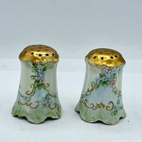 Front view of both porcelain shakers showing floral design, gilt tops and flared bases