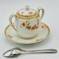 Sugar bowl with lid on matching underplate and stainless spoon in front