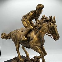 Front left view of bronze-tone horse and jockey sculpture on dark wood base