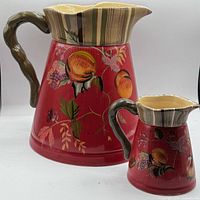 Front view of pitcher and creamer showing artwork and handles