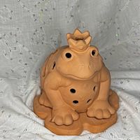 Front view of terracotta frog prince tealight holder on lily pad base showing vent holes and crown