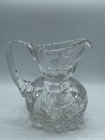 Full view of clear cut crystal pitcher showing starburst pattern and curved handle