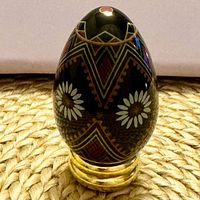 Front view of black porcelain egg on stand showing daisy motif and geometric design