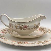 Gravy boat on drip plate showing floral pattern and gold rim.