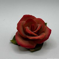 Front view of red porcelain rose figurine with green leaves
