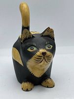 Front view of carved wooden cat figurine showing facial details and chipped ear