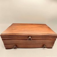 Closed wooden jewelry box front view, showing clasp and drawer pulls