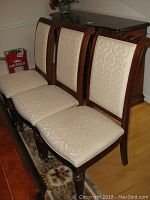 Four cream-upholstered wooden dining chairs with carved frames displayed against sideboard.