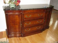 Front view of wooden buffet with black marble top, three drawers with brass handles, two side cabinets with decorative carved edges and fluted detail.