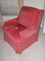 Front angled view of salmon colored overstuffed armchair showing cushioned arms, seat, and back, with skirted base.