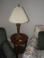 Three-legged round wooden side table with brass tone lamp on top, showing small scratch on tabletop.