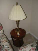 Full view of wooden round side table with brass tone lamp on top, showing table diameter and height relative to sofa and carpet floor.