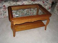 Front angle view of wooden coffee table with beveled glass insert top and lower shelf.