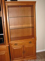 Front view of a Thomasville wooden display cabinet showing two glass shelves and overhead built-in light.