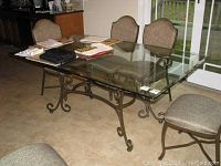 Full view of rectangular smoked beveled glass top table with rounded corners and metal base, situated in dining area with chairs.