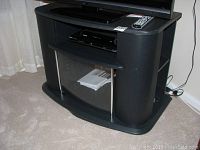 Black TV media stand with curved glass door on front and Toshiba DVD player inside open shelf, with TV remote on top.