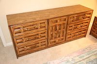 Full view of wooden dresser showing 6 drawers and 1 cabinet door front with carved geometric design