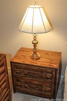 Photo of a wood dresser with two drawers and a brass table lamp on top illuminating, showing the overall look and condition.